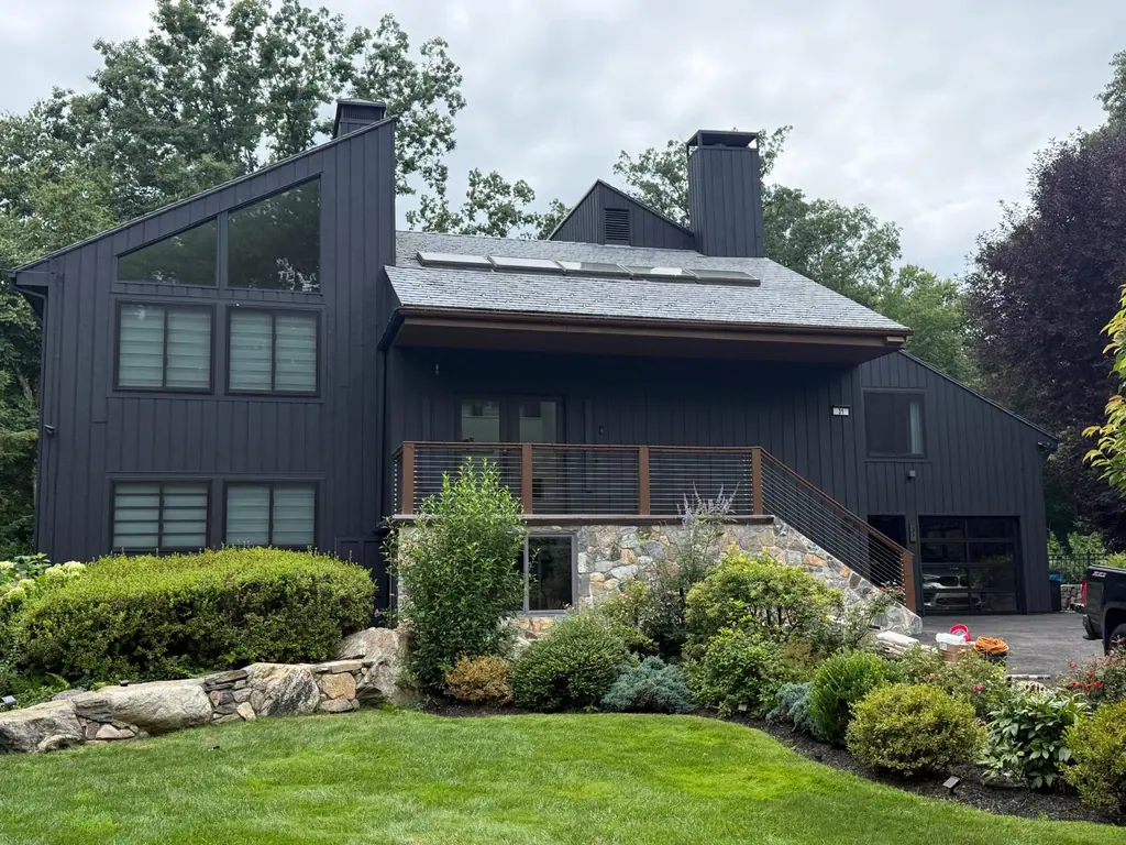 Contemporary home with vertical siding painted black, stone base and landscaped yard
