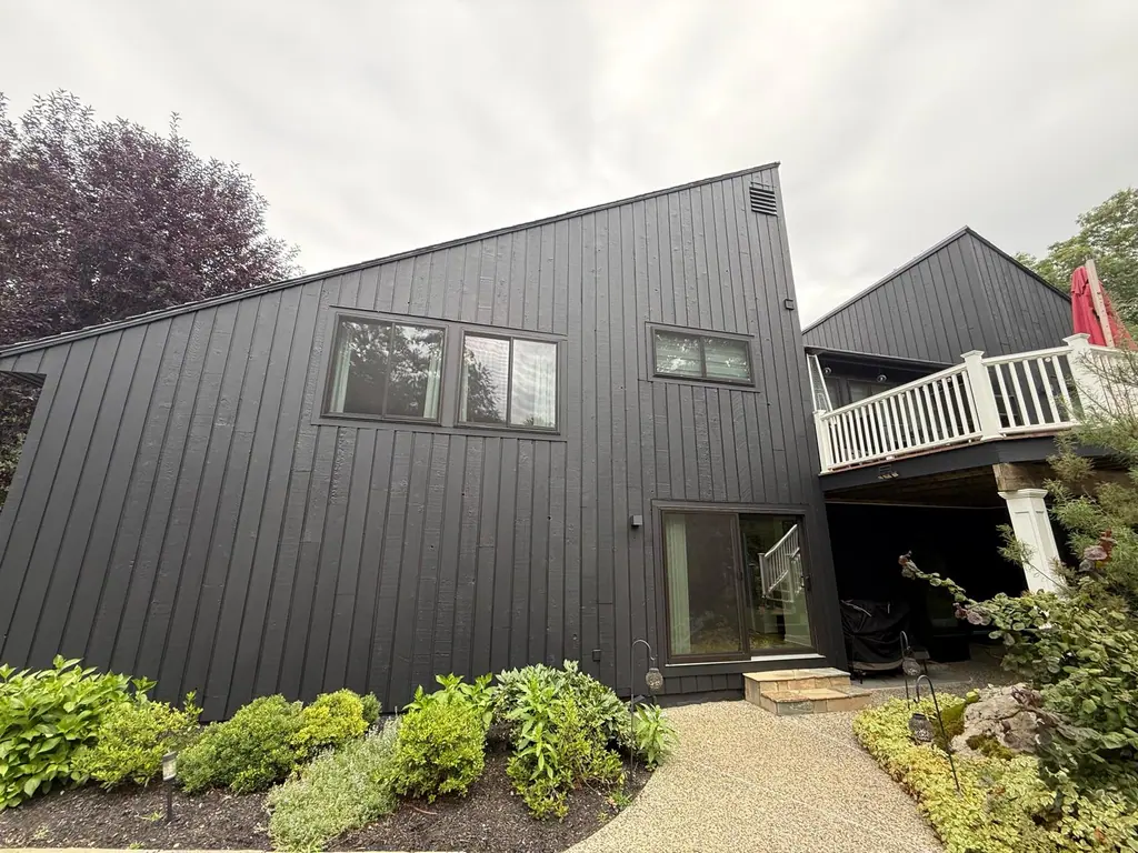 Side of a contemporary home with black painted siding and garden beds