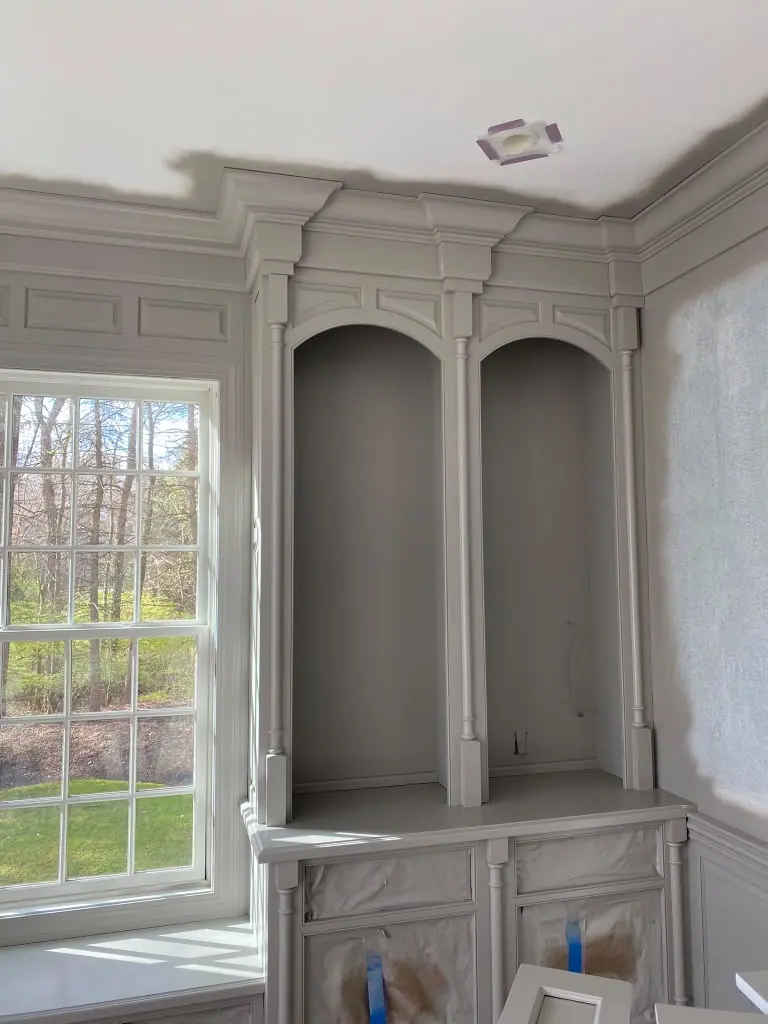 Gray painted bookcase next to a tall window